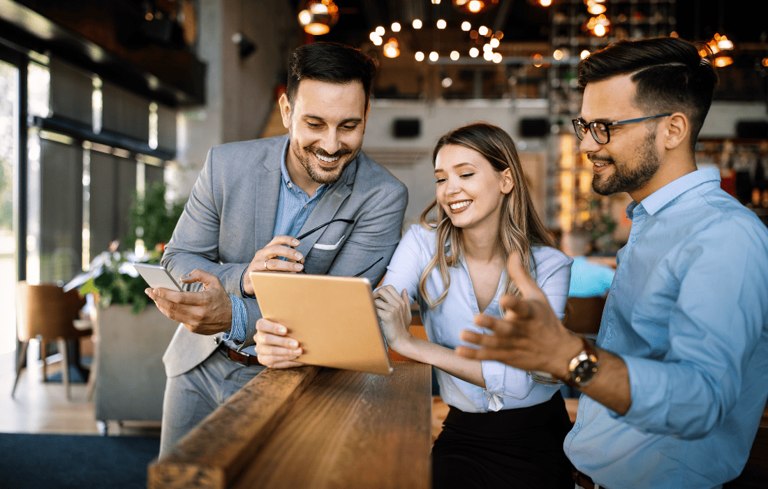 Three smiling business professionals collaborating and reviewing information on a tablet in a modern office setting