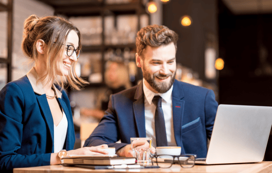 Two business professionals collaborating on laptop in modern café, discussing LMS solutions and e-learning strategies